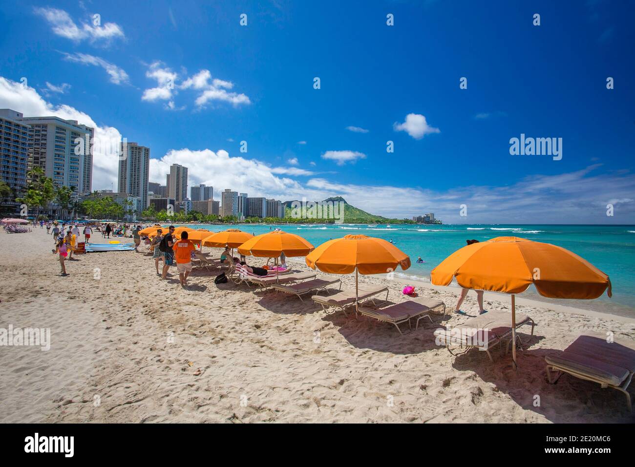 Ein Blick auf Liegestühle, Sonnenschirme und Touristen auf dem ikonischen Waikiki Strand mit Diamond Head hinter sich auf der Insel Oahu, Hawaii. Stockfoto