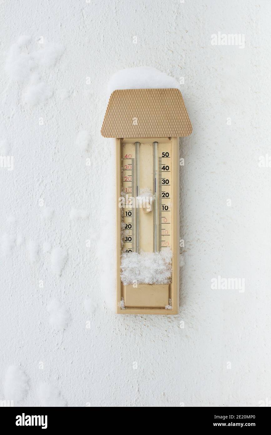Ein mit Schnee und Eis bedecktes Thermometer für den Außenbereich, das an einer weißen Wand hängt. Winter Herbst. Stockfoto