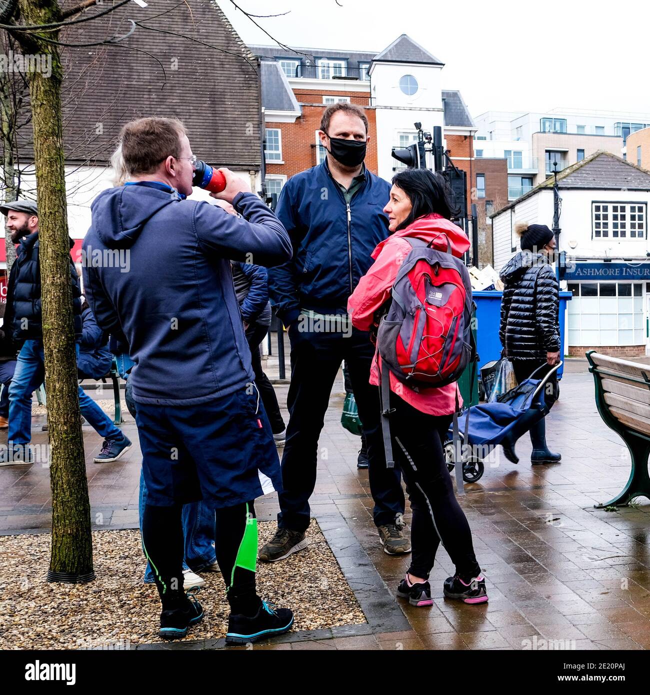 London Großbritannien, kleine Gruppe von Menschen einige tragen Schutzgesichtenmasken Trinken Takeaway Kaffee stehend Reden an EINEM Wet Winters Day während Covid-19 Loc Stockfoto
