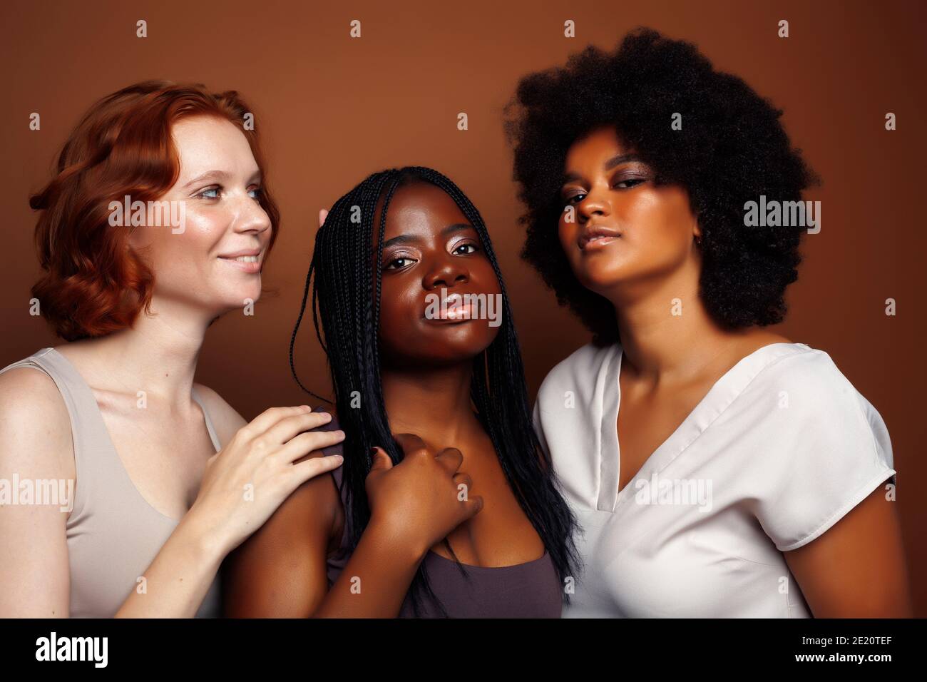 Junge hübsche kaukasische, afro, skandinavische Frau posiert fröhlich zusammen auf braunem Hintergrund, Lifestyle diverse Nationalität Menschen Konzept Stockfoto