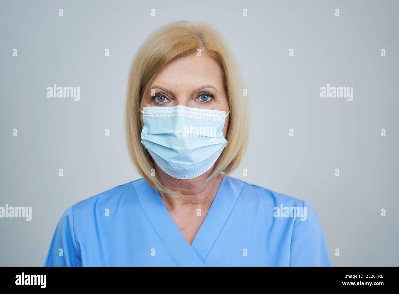 Ältere Ärztin posiert in Maske auf grauem Hintergrund Stockfoto