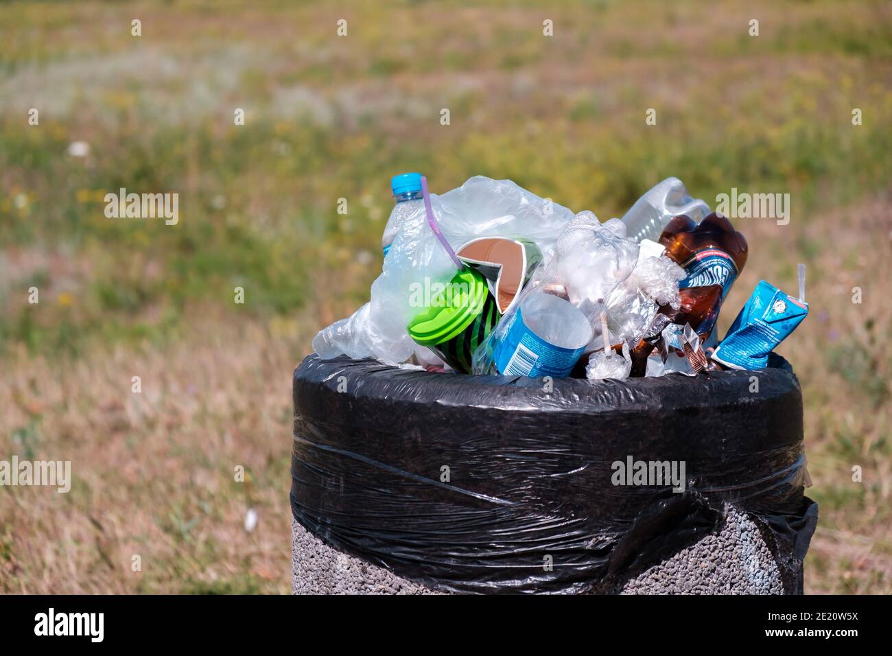 KRYVYI RIH, UKRAINE - AUGUST 2020. Plastikflaschen und Beutel in überladenen Mülltonne auf einem Gras im Stadtpark Stockfoto