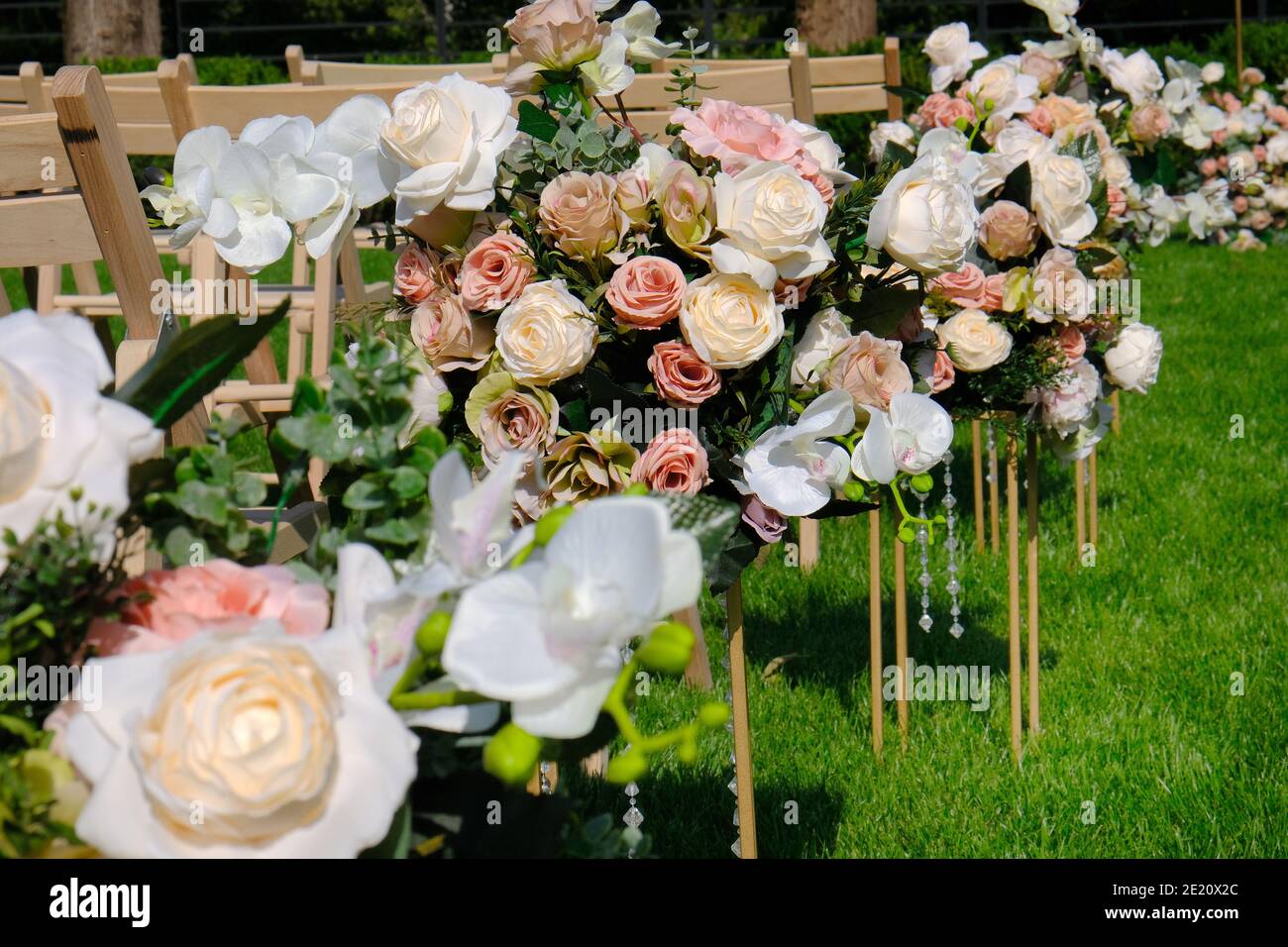 Blumensträuße und weiße leere Holzstühle auf grünem Gras. Dekoration für Hochzeitszeremonien. Stockfoto