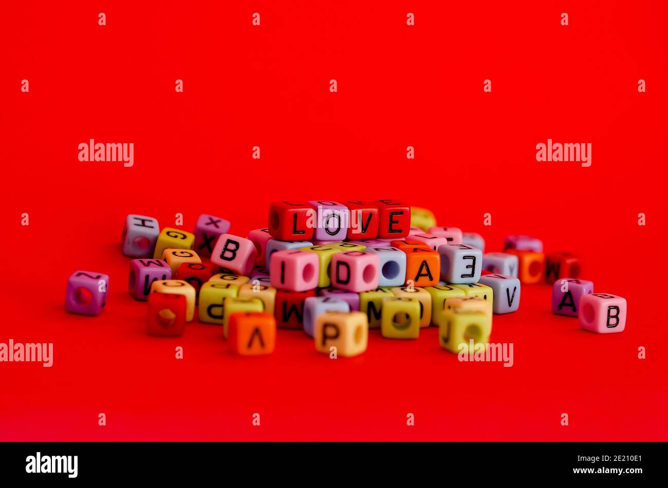Bunte Holzwürfelperlen mit Buchstaben auf rotem festlichem Hintergrund, Wort "Liebe". Valentinstag. 14 Februar. Flach liegend, Draufsicht. Stockfoto