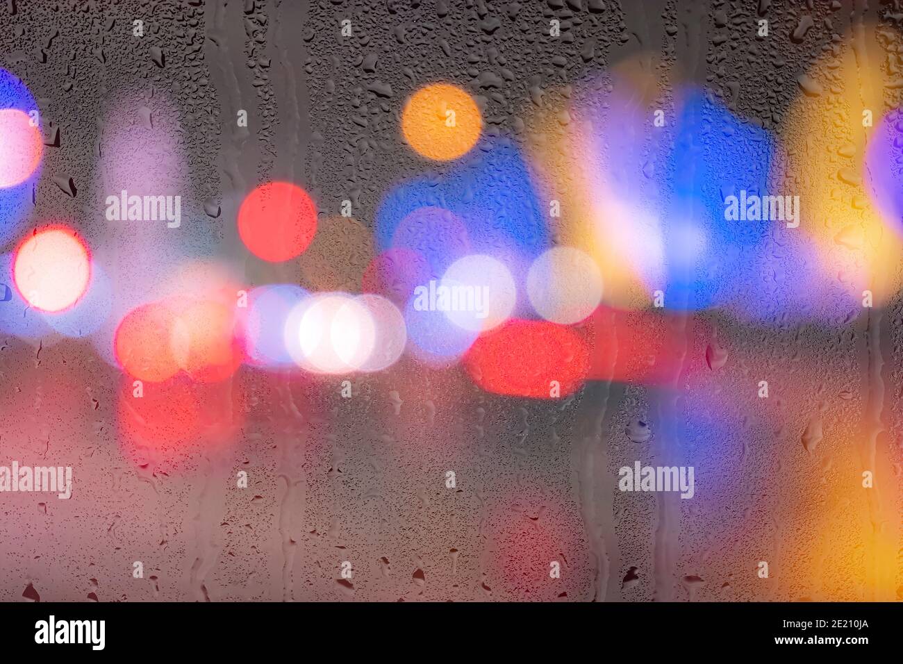 Nächtliche Stadtlichter und Autoscheinwerfer durch Regenglas. Regen und schlechtes Nass-Wetter-Konzept. Stockfoto