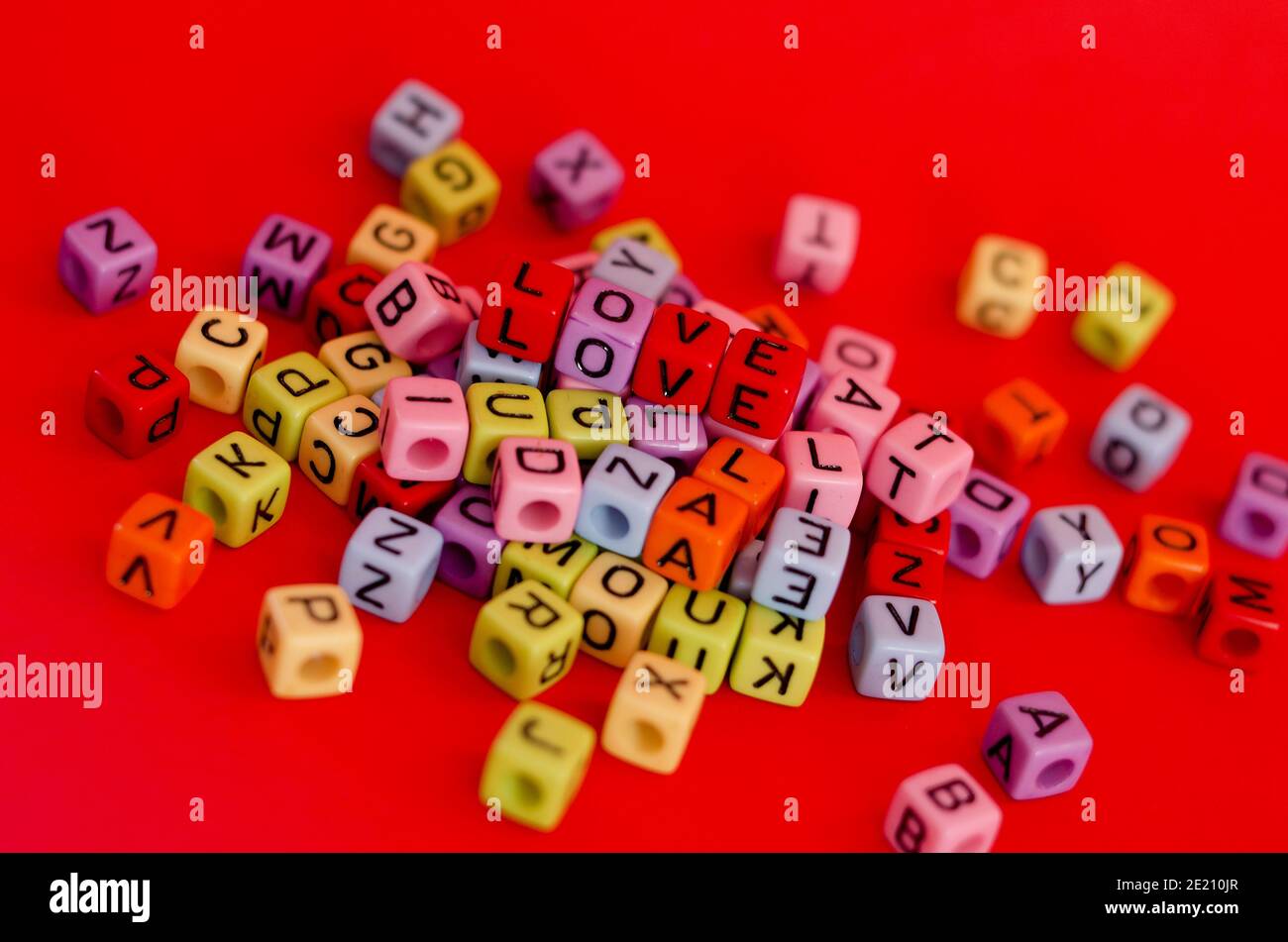 Bunte Holzwürfelperlen mit Buchstaben auf rotem festlichem Hintergrund, Wort "Liebe". Valentinstag. 14 Februar. Flach liegend, Draufsicht. Stockfoto