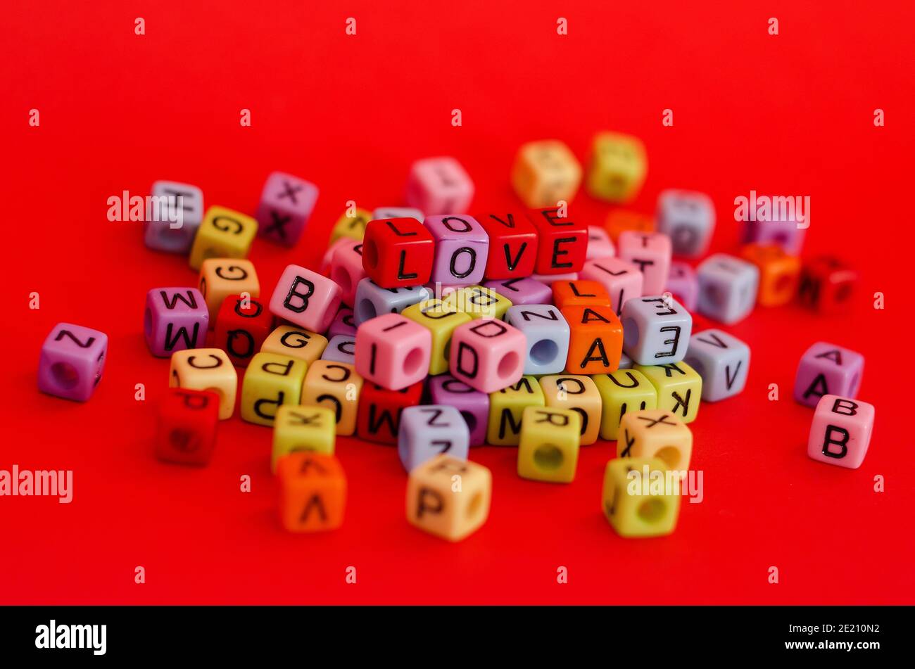 Bunte Holzwürfelperlen mit Buchstaben auf rotem festlichem Hintergrund, Wort "Liebe". Valentinstag. 14 Februar. Flach liegend, Draufsicht. Stockfoto