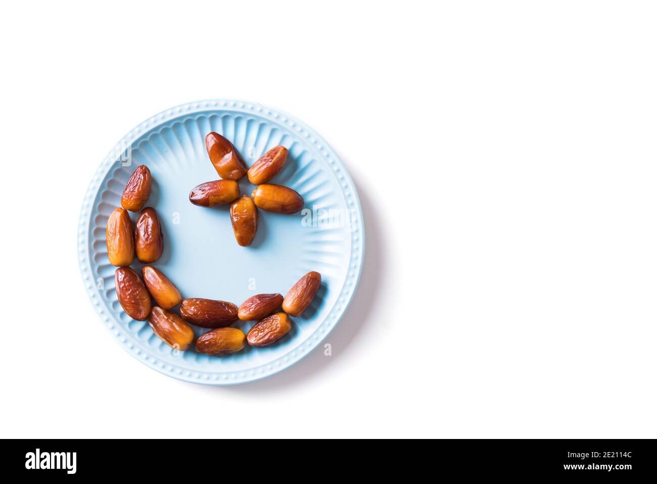 Islamischer Halbmond. Ramadan Kareem mit Datteln Früchte in Form von Halbmond auf blauer Platte isoliert auf weißem Hintergrund angeordnet, Draufsicht, Kopierraum Stockfoto