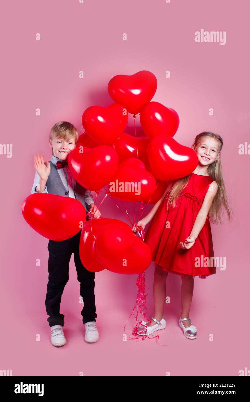 Valentinstag. Zwei glückliche Kinder mit herzförmigen Luftballons auf rosa Hintergrund Stockfoto