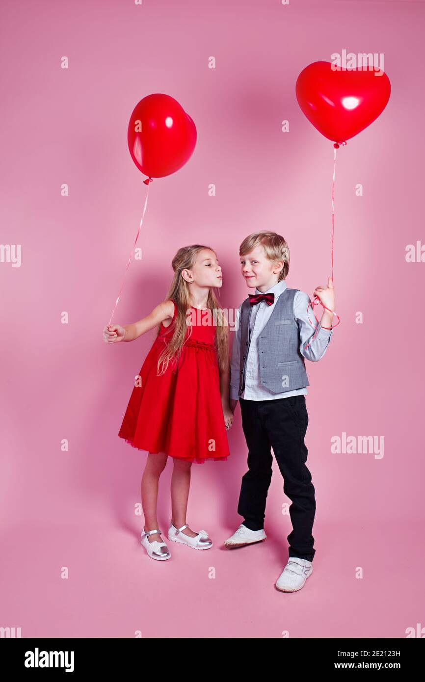 Valentinstag. Kleiner Junge küssen schöne kleine Mädchen auf rosa Hintergrund. Kinder mit Herzballons Stockfoto