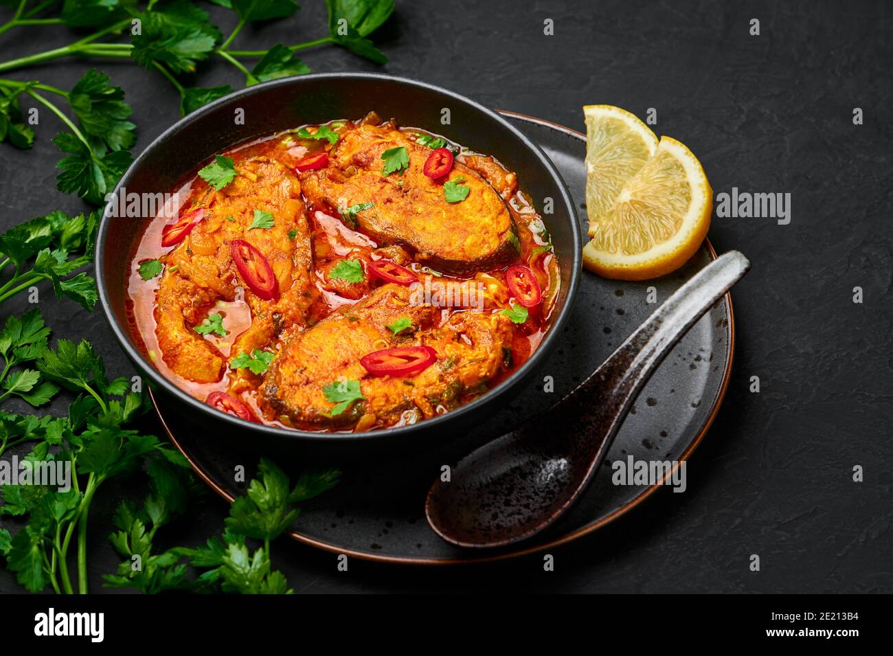 Macher Jhol in schwarzer Schale auf dunkler Schieferplatte. Indische Küche Bengalischer Fisch Curry. Asiatische Speisen und Gerichte. Stockfoto