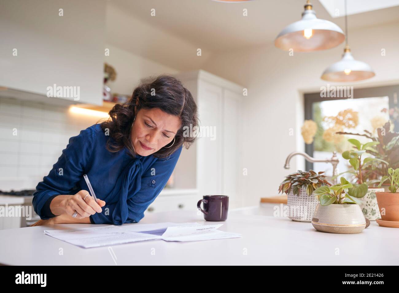 Reife Frau Überprüfung Und Unterzeichnung Inländischen Finanzen Und Investitionen Papierkram In Der Küche Zu Hause Stockfoto