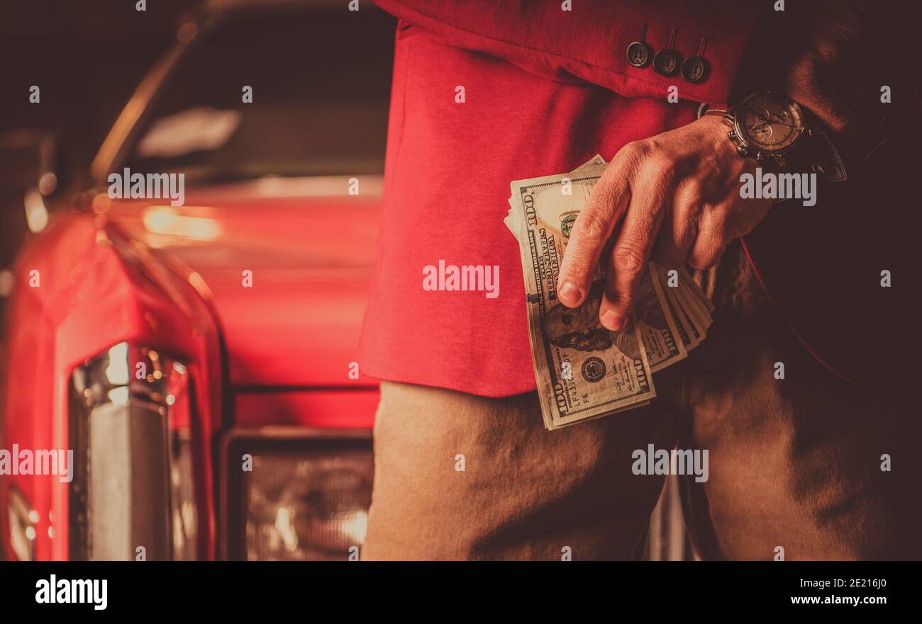Elegante Männer tragen Burgunder Anzug mit Haufen von Cash Money American Dollars. Red Classic Car im Hintergrund. Stockfoto