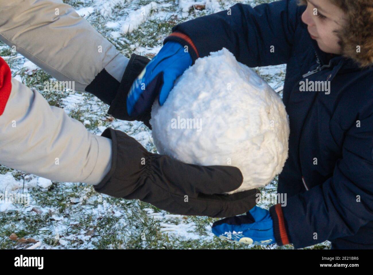 Hände eines Teenagers und eines kleinen Kindes, das einen hält Großer Schneeball an einem kalten Wintertag Stockfoto