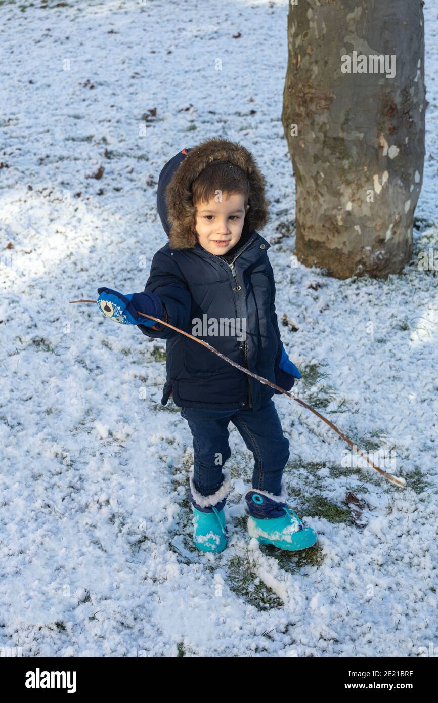 Selektiver Fokus auf ein warmes, nur mit Stiefeln bespieltes Kleinkind mit Schnee und einem Stock an einem Wintertag Stockfoto