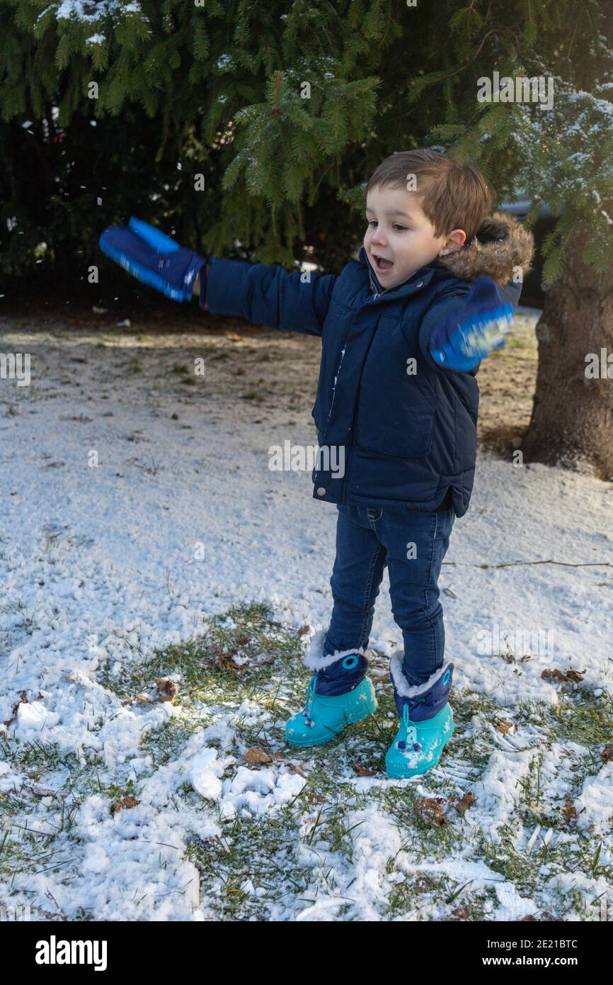Selektive Fokussierung eines warm gekleideten Kleinkindes in Handschuhen und Stiefel genießen den Schnee mit ausgestreckten Armen Stockfoto