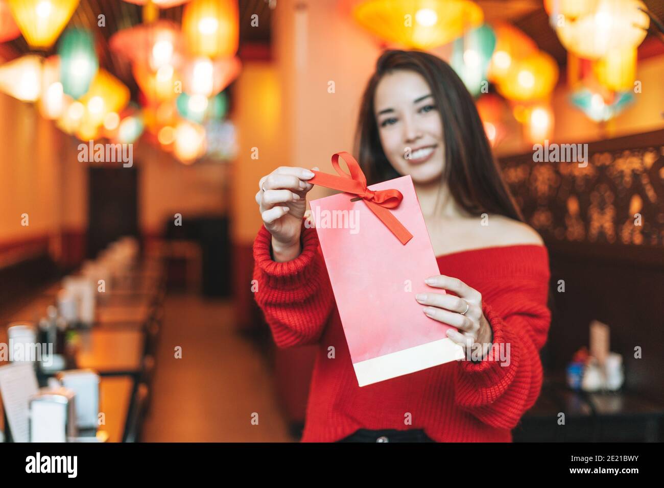 Schöne junge asiatische Frau in roten Kleidern mit rotem Geschenk Tasche im Restaurant zur Feier des chinesischen Neujahrs Stockfoto