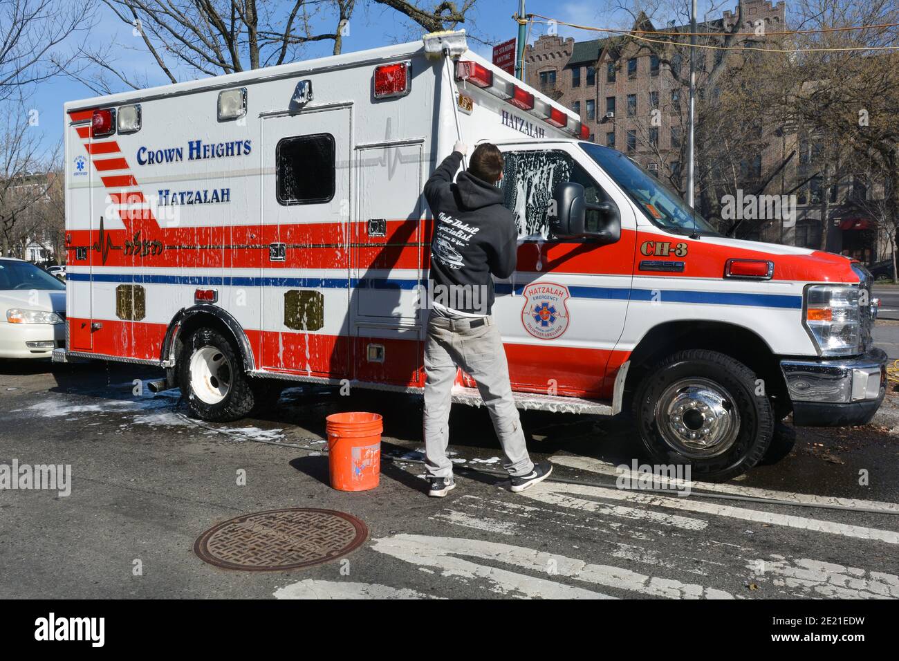 Ein junger Mann wäscht einen Hatzalah Krankenwagen auf dem Eastern Parkway in Crown Heights, Brooklyn, New York City außerhalb des Lubavitch Hauptquartiers. Stockfoto