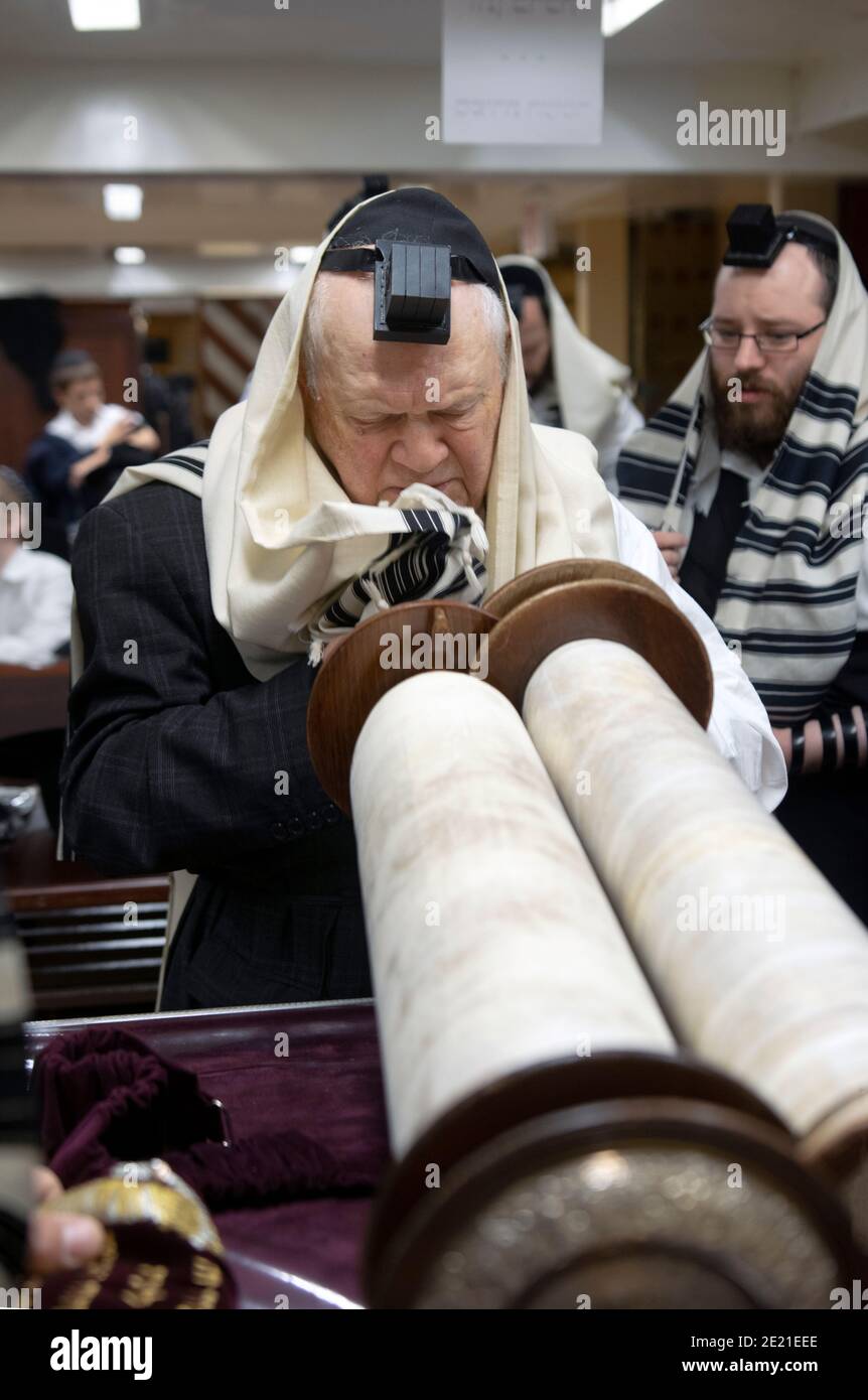 Ein älterer orthodoxer jüdischer Mann hebt die Tora leicht an, nachdem er an Wochentagen morgens zum Lesen gerufen wurde. In Crown Heights, Brooklyn. Stockfoto
