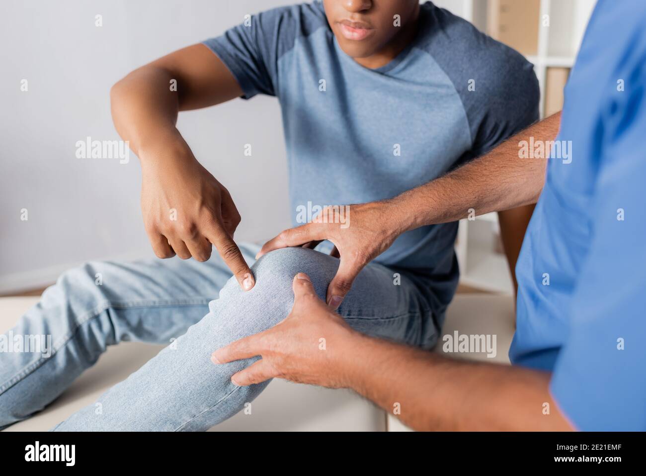 Zugeschnittene Ansicht eines afroamerikanischen Patienten, der mit dem Finger auf den Patienten zeigt Knie in der Nähe des Arztes Stockfoto