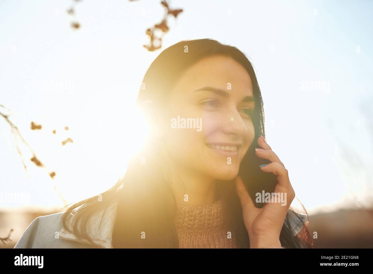 Nahaufnahme Porträt einer lächelnden jungen Frau hält sie Smartphone in der Nähe des Ohrs im Freien an einem warmen Herbstabend Stockfoto