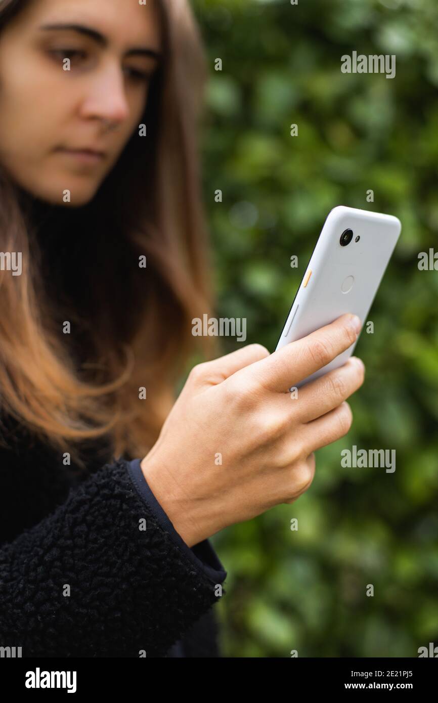Junge Frau mit langen braunen Haaren und schwarzen Jacke Texting Auf weißem Smartphone Stockfoto