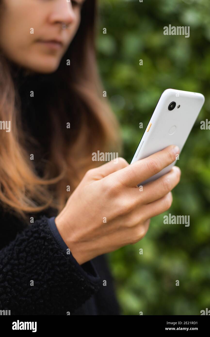 Junge Frau mit langen braunen Haaren und schwarzen Jacke Texting Auf weißem Smartphone Stockfoto