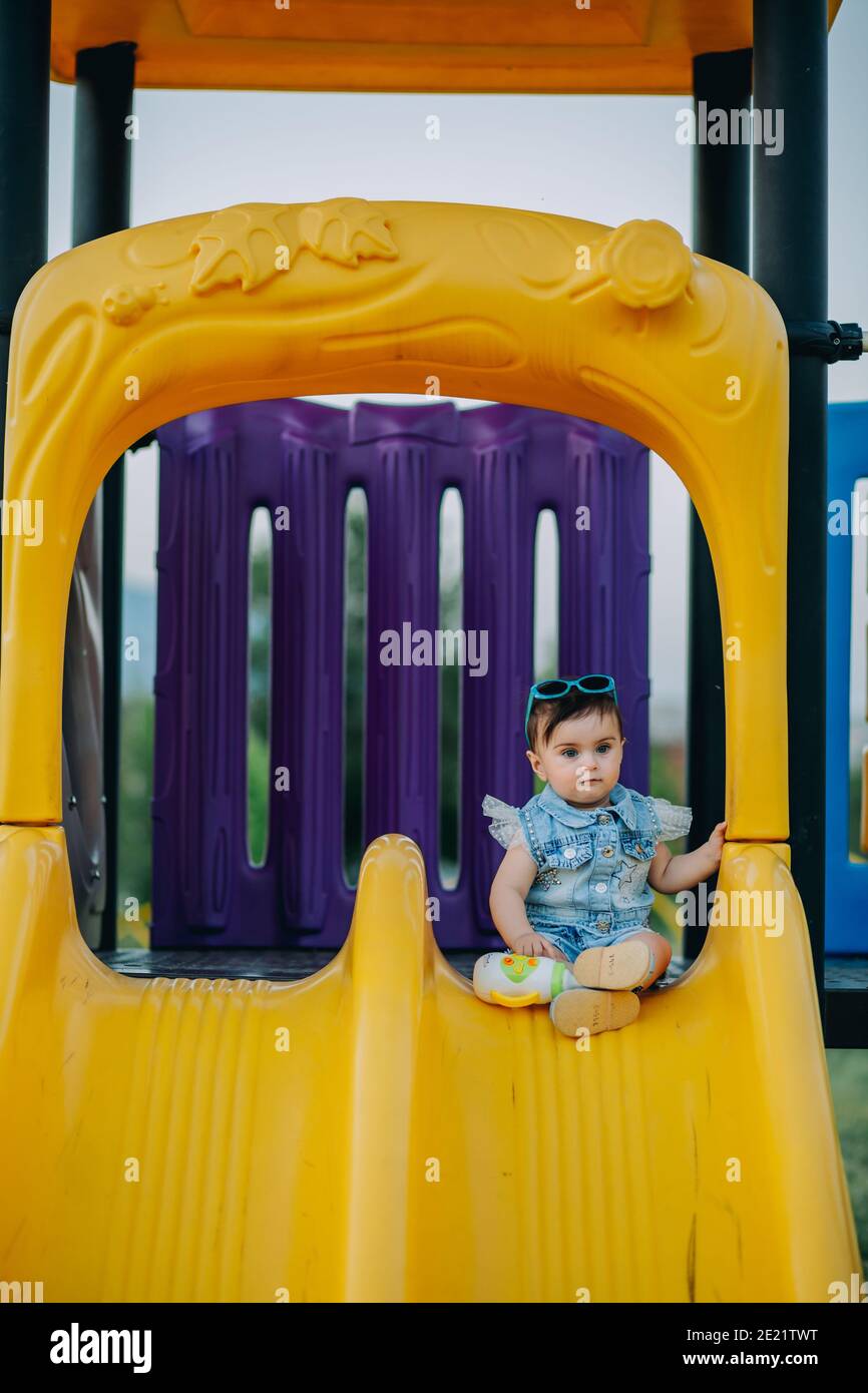 Neun Monate alt bezaubernd Baby sitzend und posiert auf gelb Rutsche auf dem Spielplatz Stockfoto