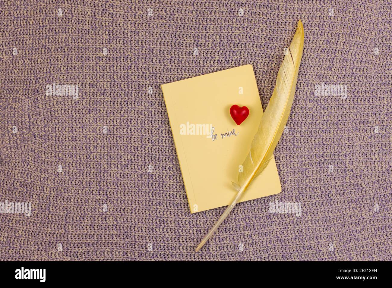 Valentinstag Grußkarte Hintergrund auf Strickpullover und Text Be meins, Komposition mit rotem Herz, Notizbuch und farbiger Feder. Hochwertige p Stockfoto