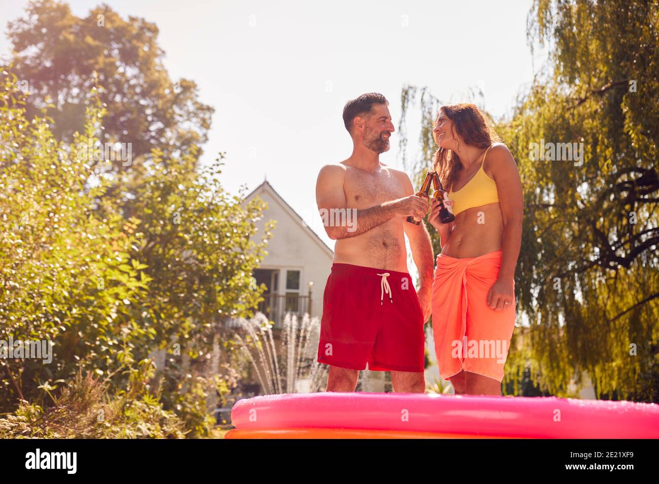 Paar Tragen Badekostüme Stehen Im Paddling Pool Im Sommer Garten Zu Hause Bier Trinken Stockfoto