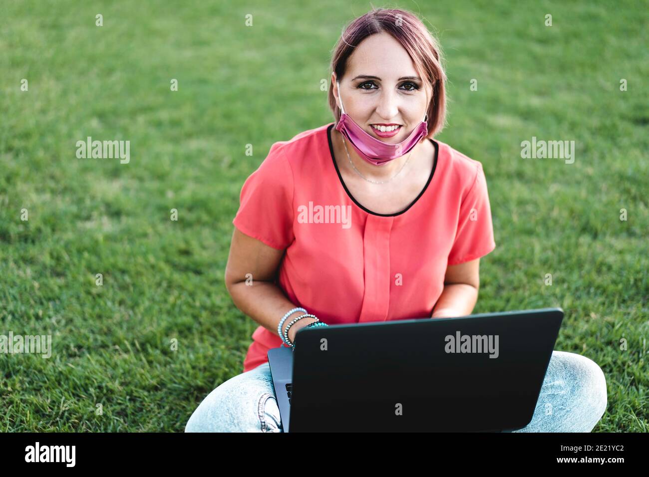 Frau 40 Jahre alt arbeitet im Freien mit Laptop während Coronavirus Outbreak - lächelnde weibliche Unternehmer sitzen auf Rasen mit persönlichen Während des Computers Stockfoto