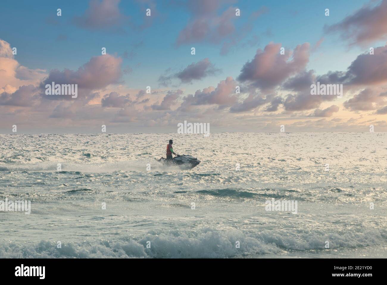 Ein Tourist auf einem Jet-Ski segelt in der Nähe des Strandes in Playa del Carmen, Mexiko. Im Hintergrund der Sonnenuntergang Himmel und das helle Meer Stockfoto
