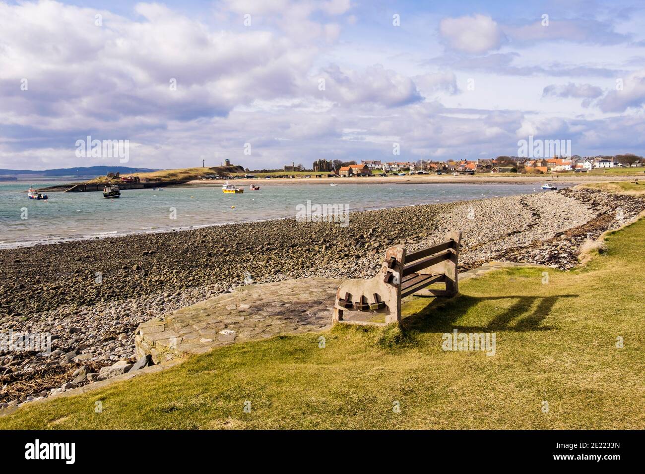 Leere Bank mit Blick auf das Meer und auf das Dorf. Lindisfarne, Holy Island, Northumberland, England, Großbritannien Stockfoto