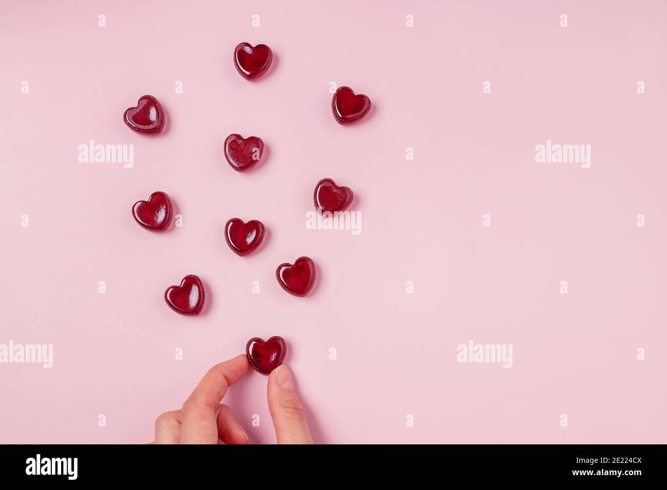 Hand hält eine der verstreuten roten Gelee Bonbons des Herzens Form auf rosa Hintergrund Stockfoto