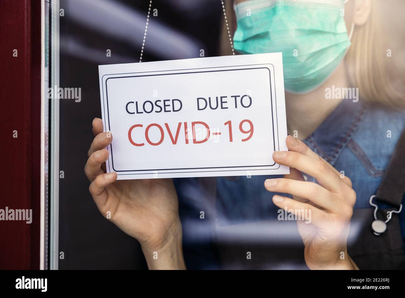 Inhaber eines kleinen Unternehmens mit Gesichtsmaske, die ein geschlossenes Schild aufmacht Schaufenster wegen Covid-19 Stockfoto