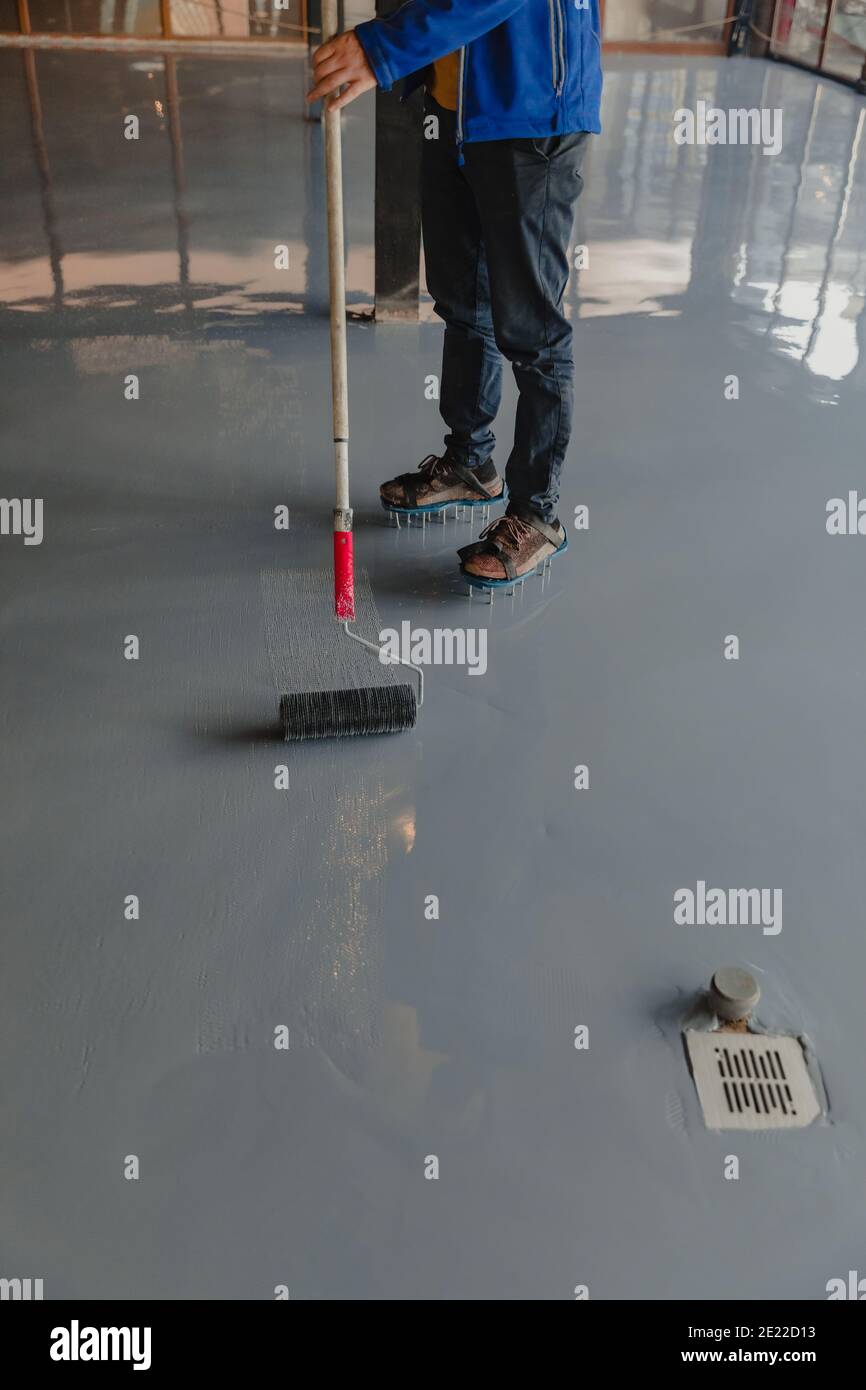 Der Arbeiter trägt graues Epoxidharz auf den neuen Boden auf Stockfoto