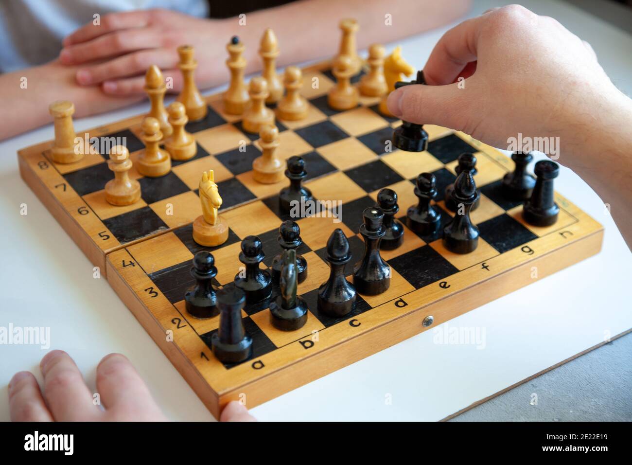 Brettspiel zu Hause. Ein Kind spielt alleine Schach. Altes Holzschachbrett. Kinderhände. Schachfiguren auf einem Schachbrett. Stockfoto