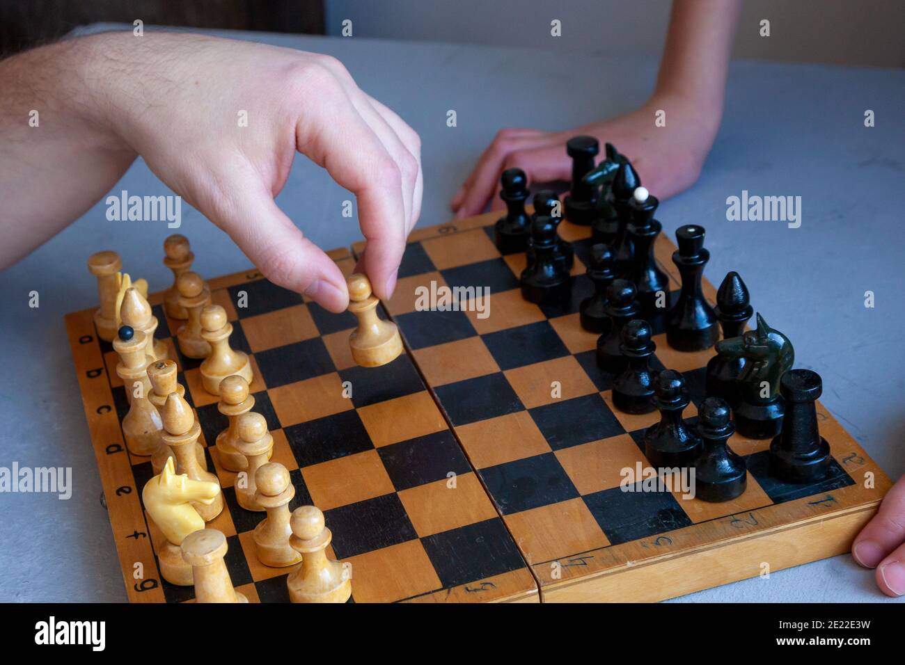 Brettspiel zu Hause. Ein Kind spielt alleine Schach. Altes Holzschachbrett. Kinderhände. Schachfiguren auf einem Schachbrett. Stockfoto