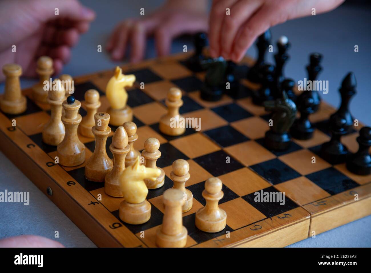 Brettspiel zu Hause. Ein Kind spielt alleine Schach. Altes Holzschachbrett. Kinderhände. Schachfiguren auf einem Schachbrett. Stockfoto