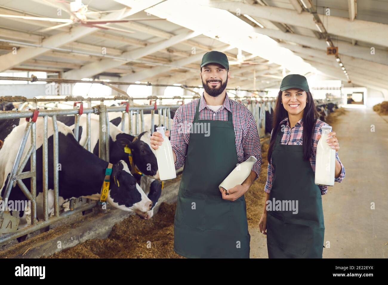 Ein paar junge Bauern halten Glasflaschen mit frischer, köstlicher Bio-Milch auf dem Bauernhof. Stockfoto
