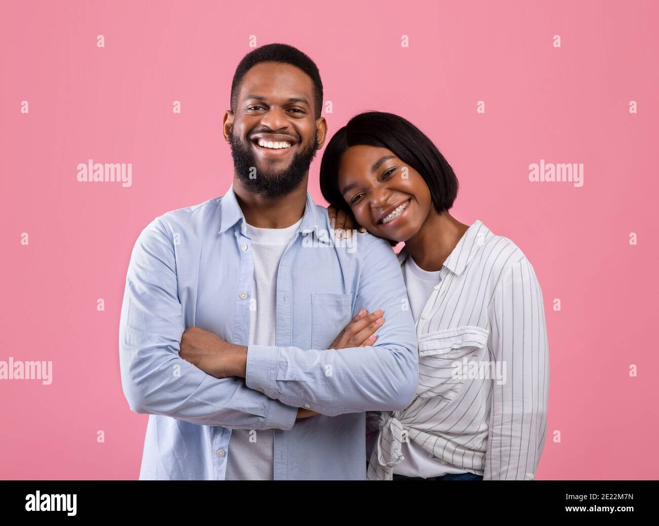 Zarte schwarze Frau, die sich auf die Schulter ihres Freundes lehnte, lächelte und die Kamera auf dem rosa Studiohintergrund ansah Stockfoto