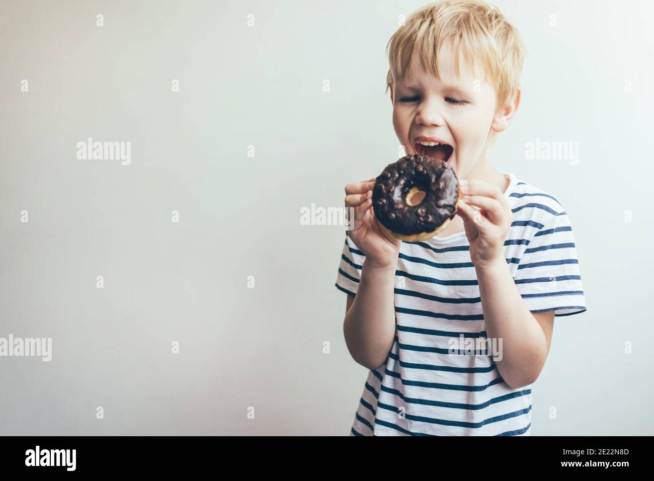 Teen junge beißt ein Schokolade Donut. Lustige Porträt eines Kindes. Stockfoto