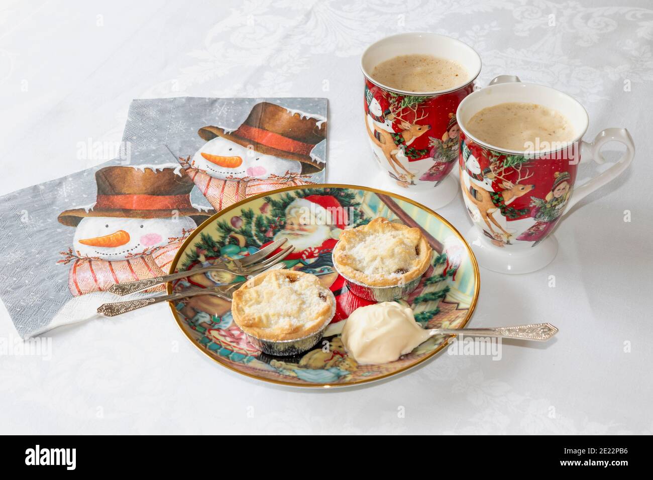 Zwei hausgemachte Mince Pies auf Weihnachtsteller mit Löffel frischer Sahne, neben zwei Tassen cremigen Kaffee und Servietten. Komfort Essen im Winter Stockfoto