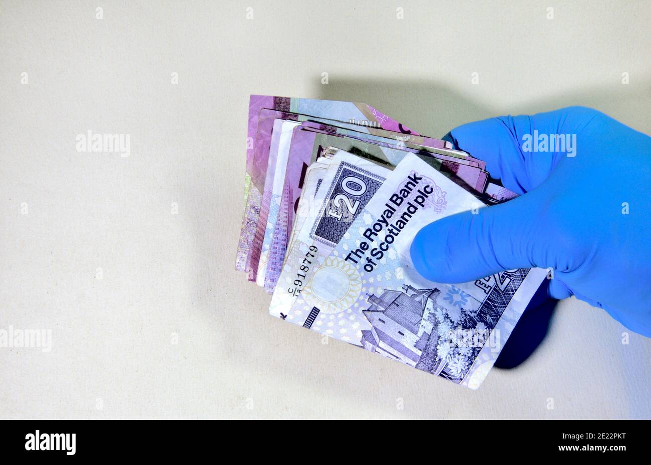 Hand in schützenden Gummihandschuh hält Haufen von britischem Geld, schottischen, Papier-Notizen Stockfoto