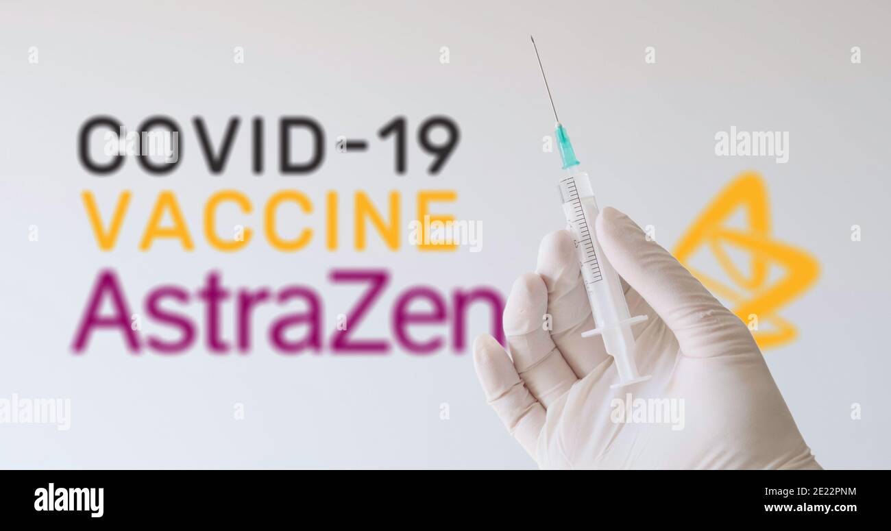 Eine Hand mit Handschuh, die eine Spritze vor dem AstraZeneca-Logo hält, einem der Unternehmen, das einen Covid-19-Impfstoff (Coronavirus) herstellt. Wien, Österreich - Jan Stockfoto