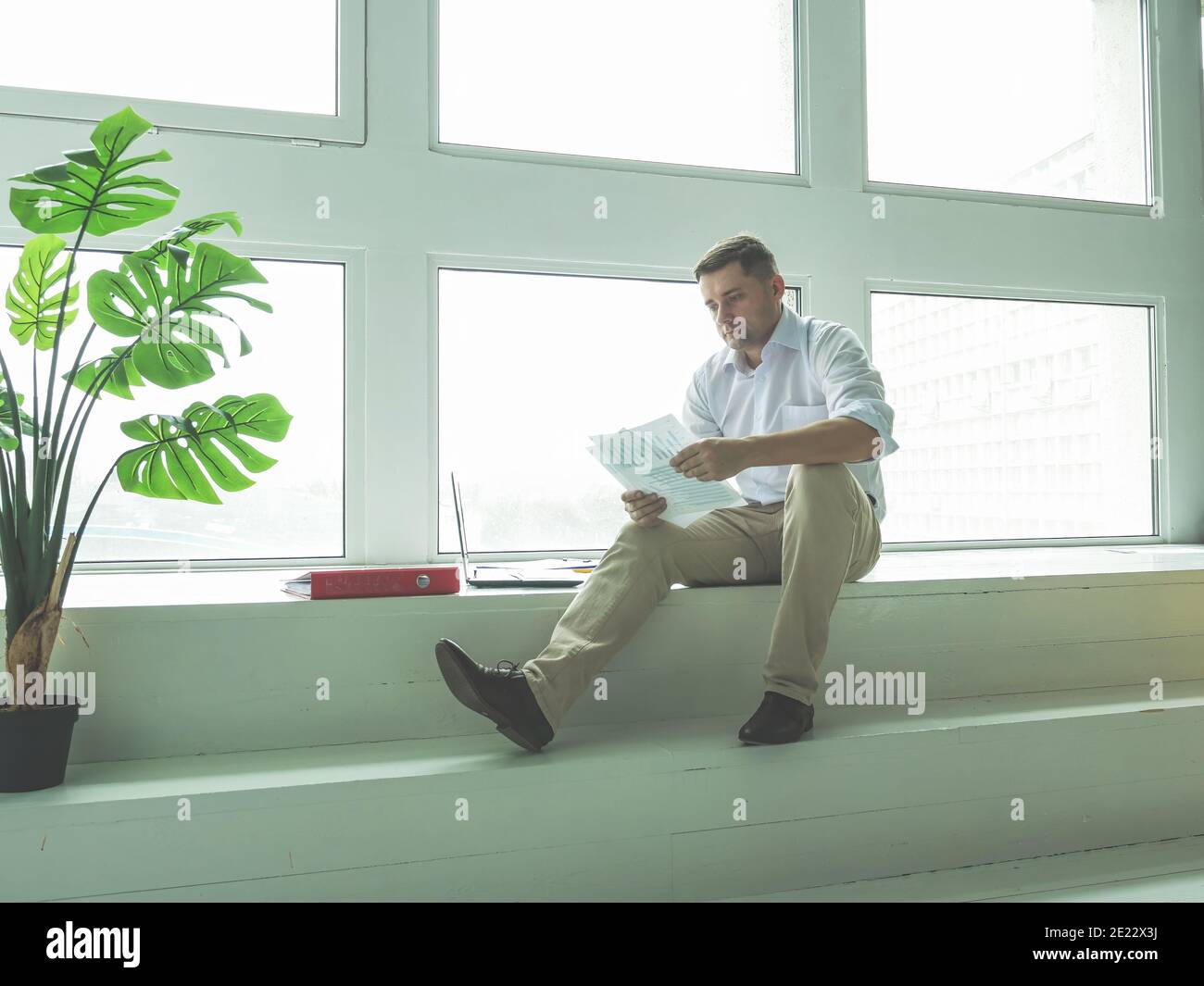 Männlicher Geschäftsmann arbeitet mit Dokumenten, während er am Fenster sitzt. Stockfoto