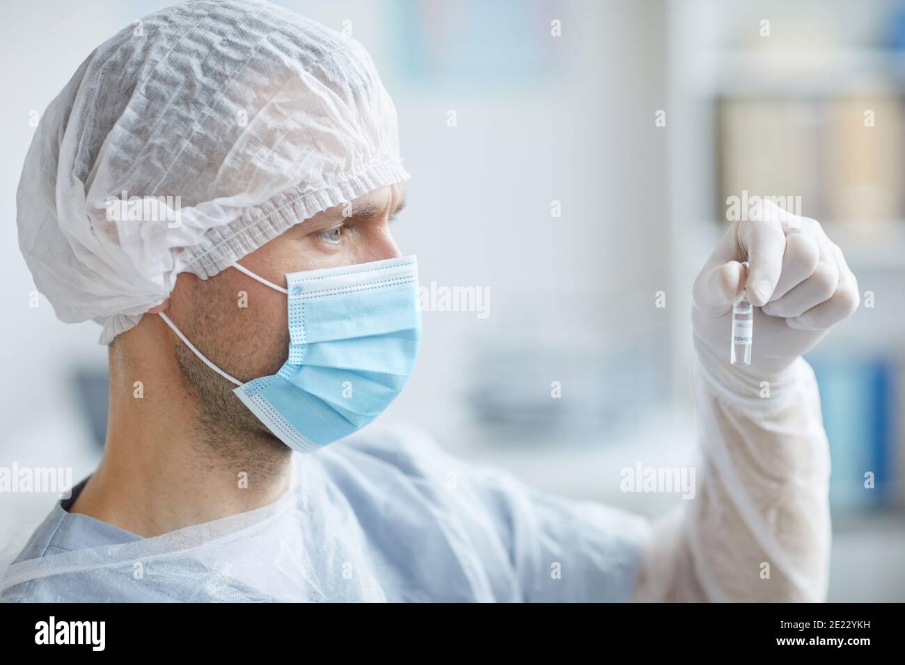 Seitenansicht Porträt der männlichen Krankenschwester trägt Maske und Schutzkleidung mit Ampulle mit Medizin während der Arbeit in der Klinik oder Krankenhaus, kopieren Raum Stockfoto