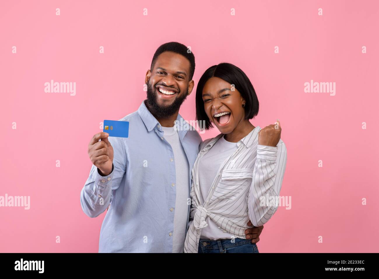 Aufgeregt schwarzes Paar mit Kreditkarte, die ja Geste macht, Förderung kontaktloses Einkaufen über rosa Studio Hintergrund Stockfoto