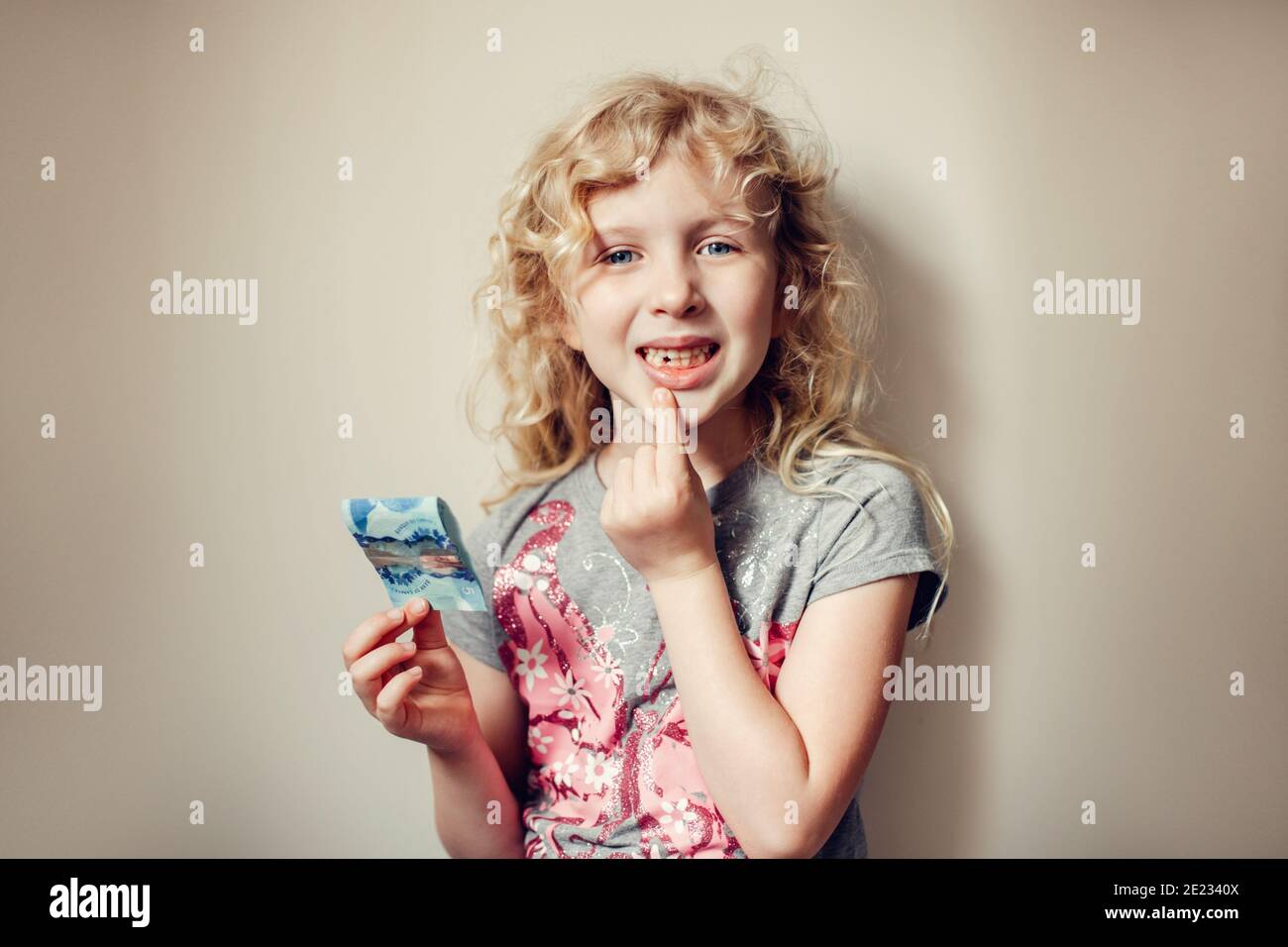 Kaukasische blonde Mädchen zeigt ihren fehlenden Zahn im Mund und hält Geld von Zahnfee. Stolzes Kind Kind zeigt verlorenen Zahn. Aufwachsen Bühne und Stockfoto