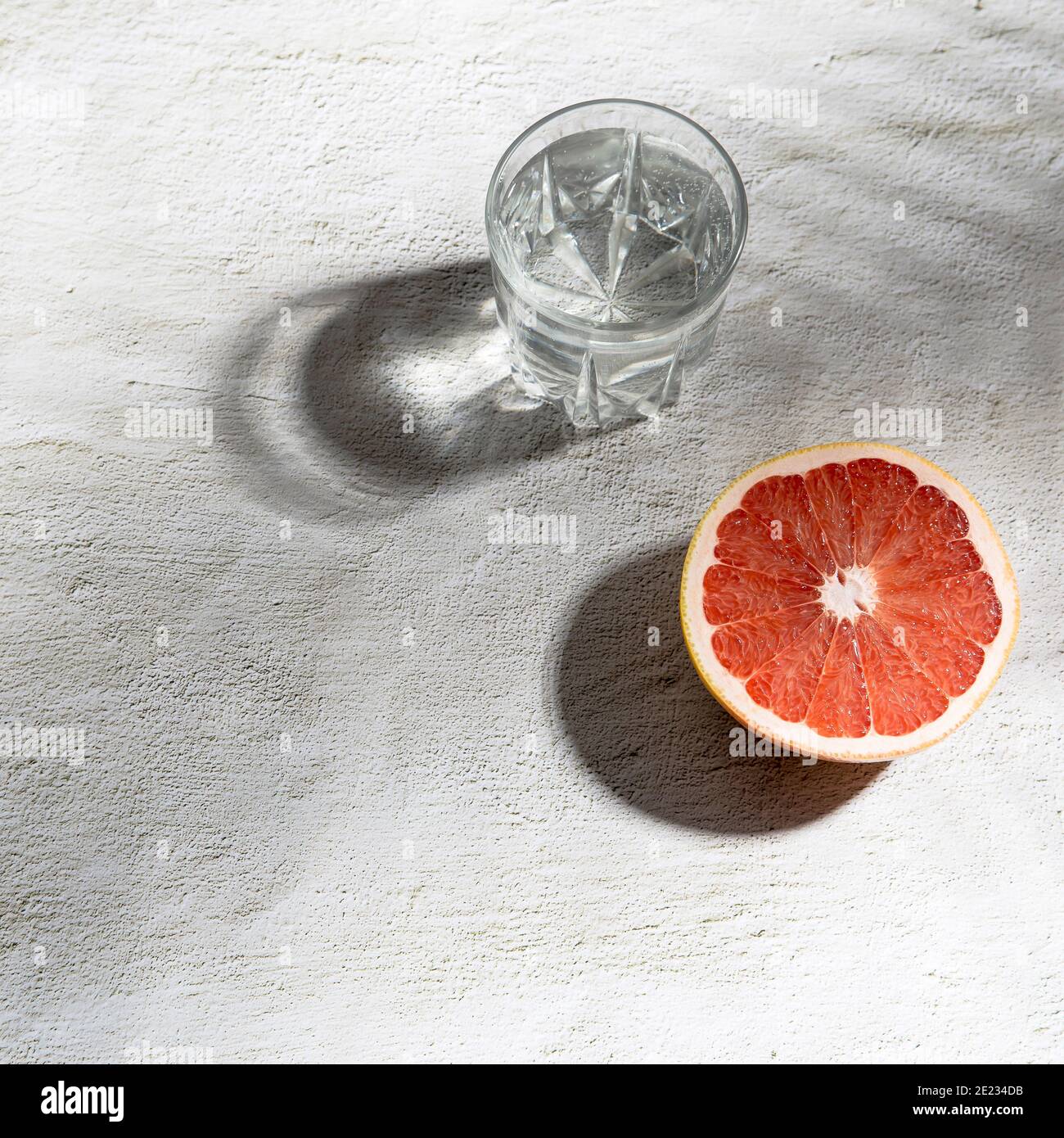 Sommer Schreibwaren Stillleben Szene. Nahaufnahme von geschnittenen Grapefruitfrüchten auf weißem Tischhintergrund im Sonnenlicht. Leere Papierkarten, Einladungen Mockup Szene Stockfoto